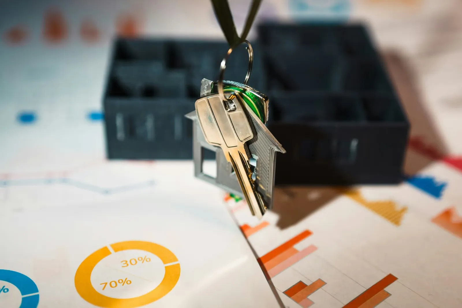 House keys on a house-shaped keyring above financial charts